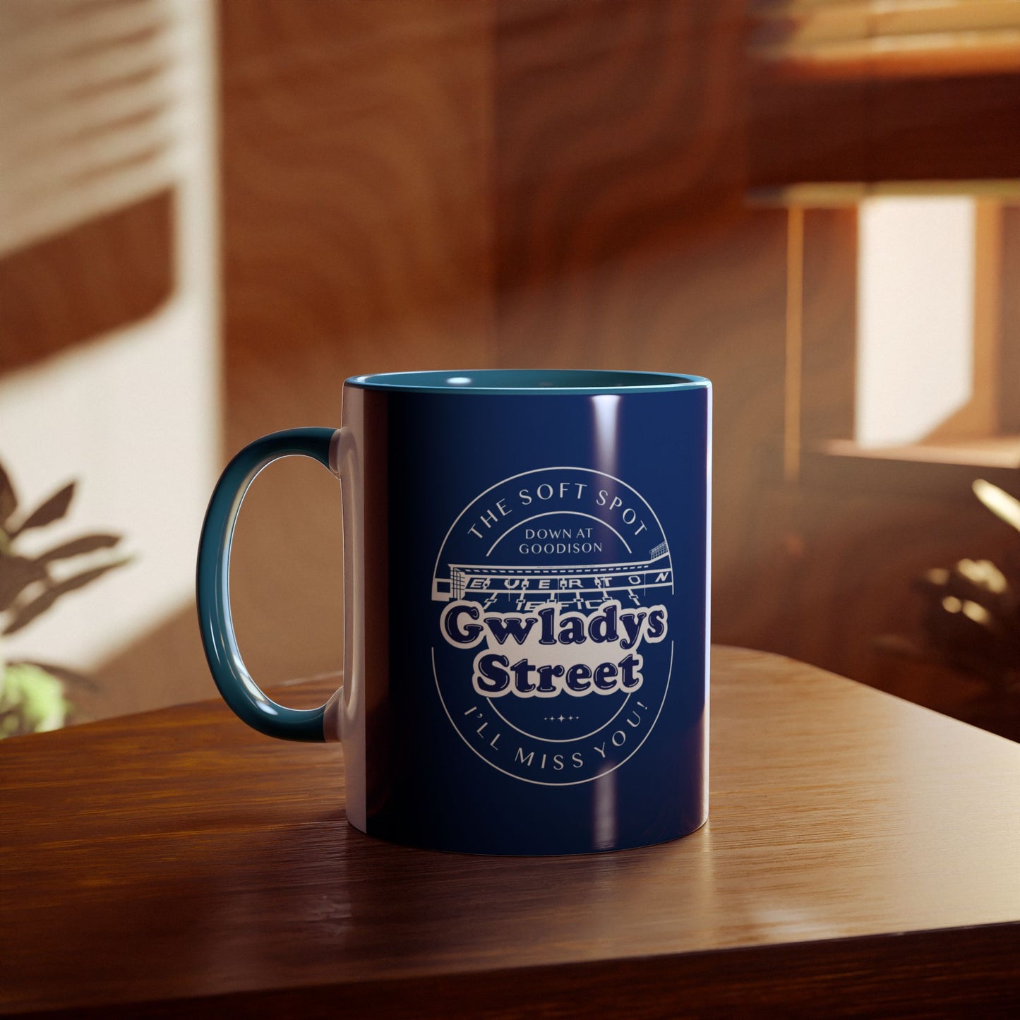 Lifestyle image showing the Navy blue and light blue mug on a wooden table with a blurred living room environment in the background you can see sunlight coming through a window and part of a house plant