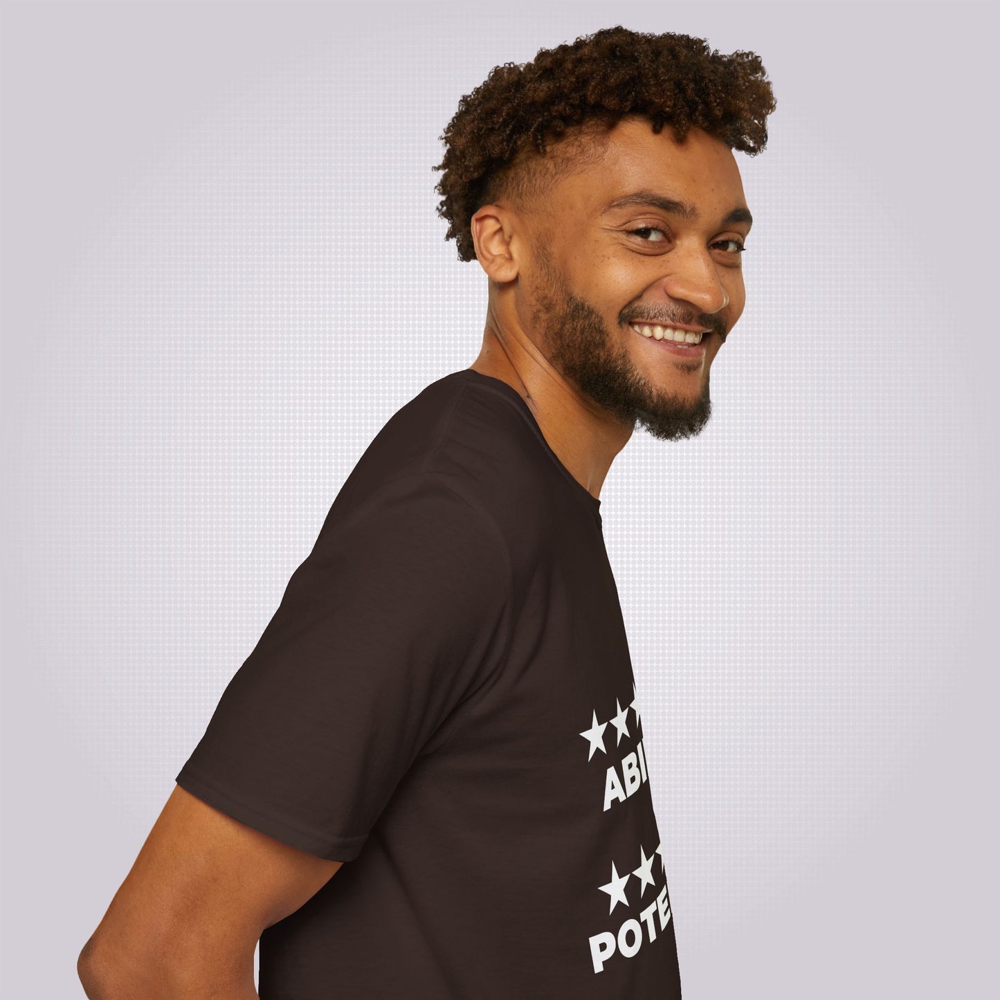 Side profile picture featuring a young mixed race male in his twenties his body is facing to the right as you look but his head is turned towards the camera and he is wearing the brown t shirt