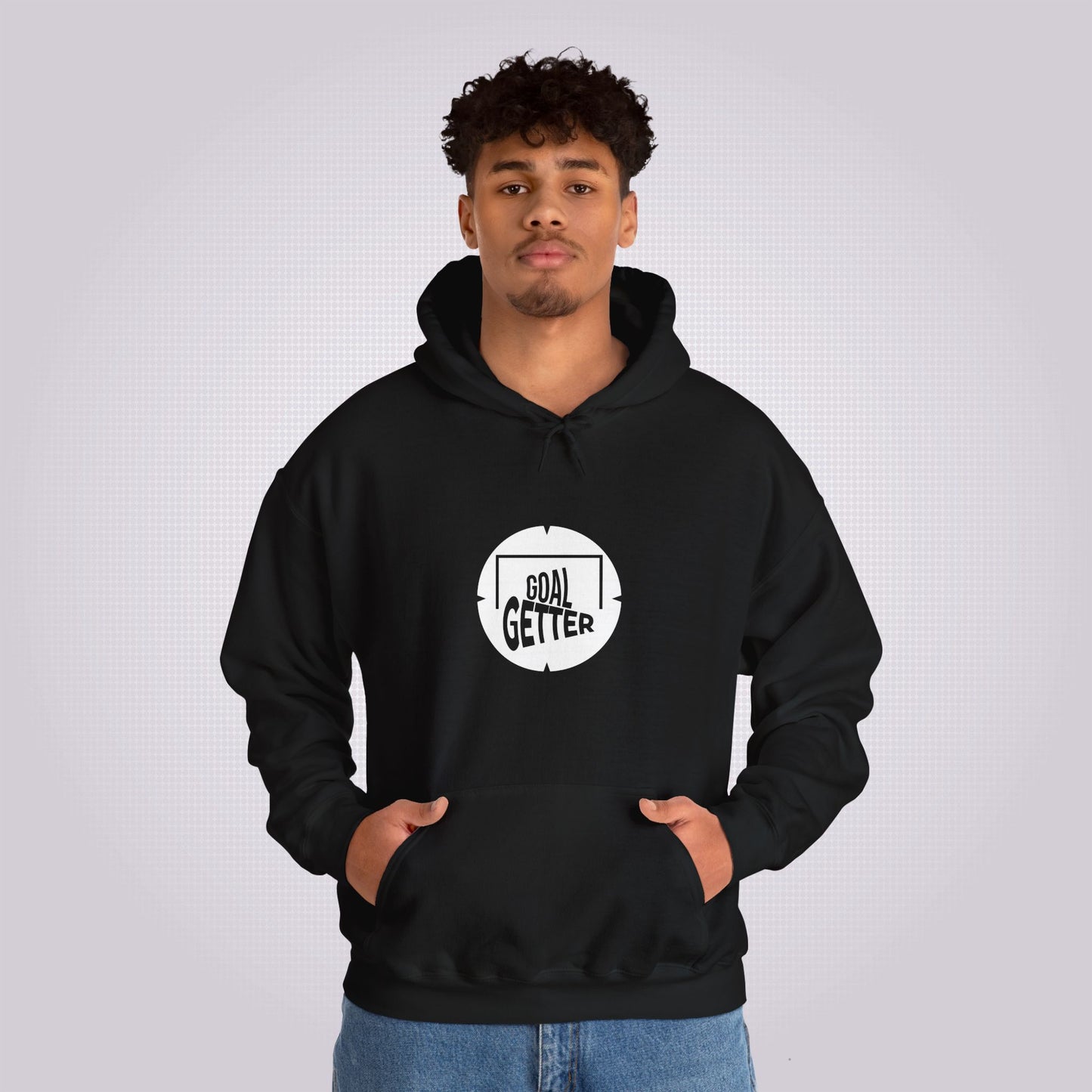 Young mixed race man looks straight at camera as he models the black hoodie and jeans he has his hands in his pockets to demonstrate the pouch design
