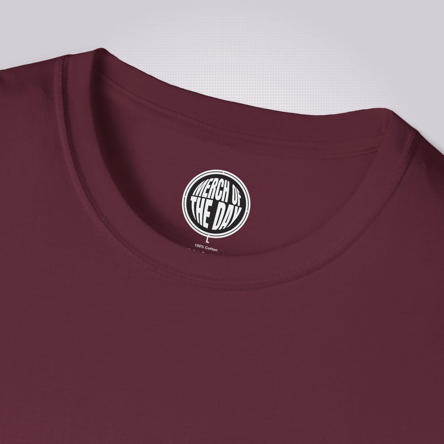 Close up of maroon t shirt on a light grey dotted background with the clothing brand logo on the inner neck label