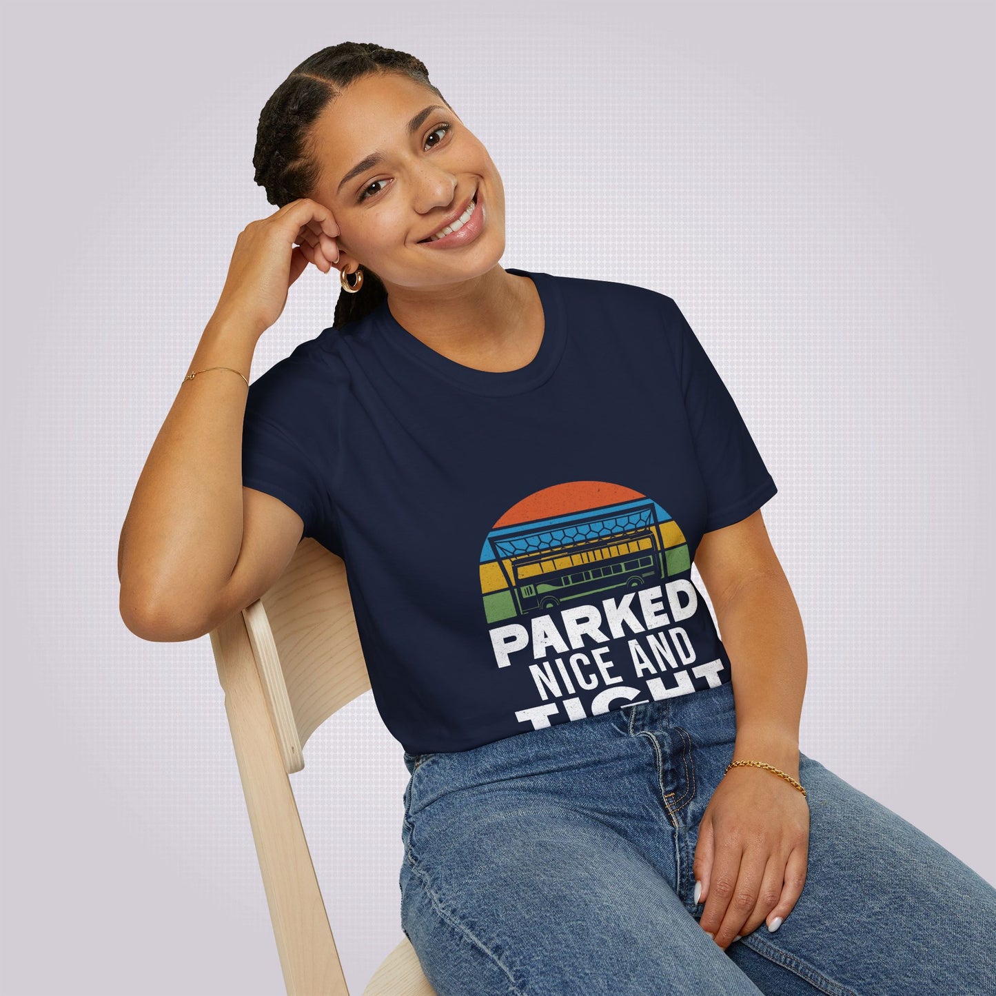 Young woman sits on a pine chair leaning on her elbow wearing the navy t shirt with a pair of jeans