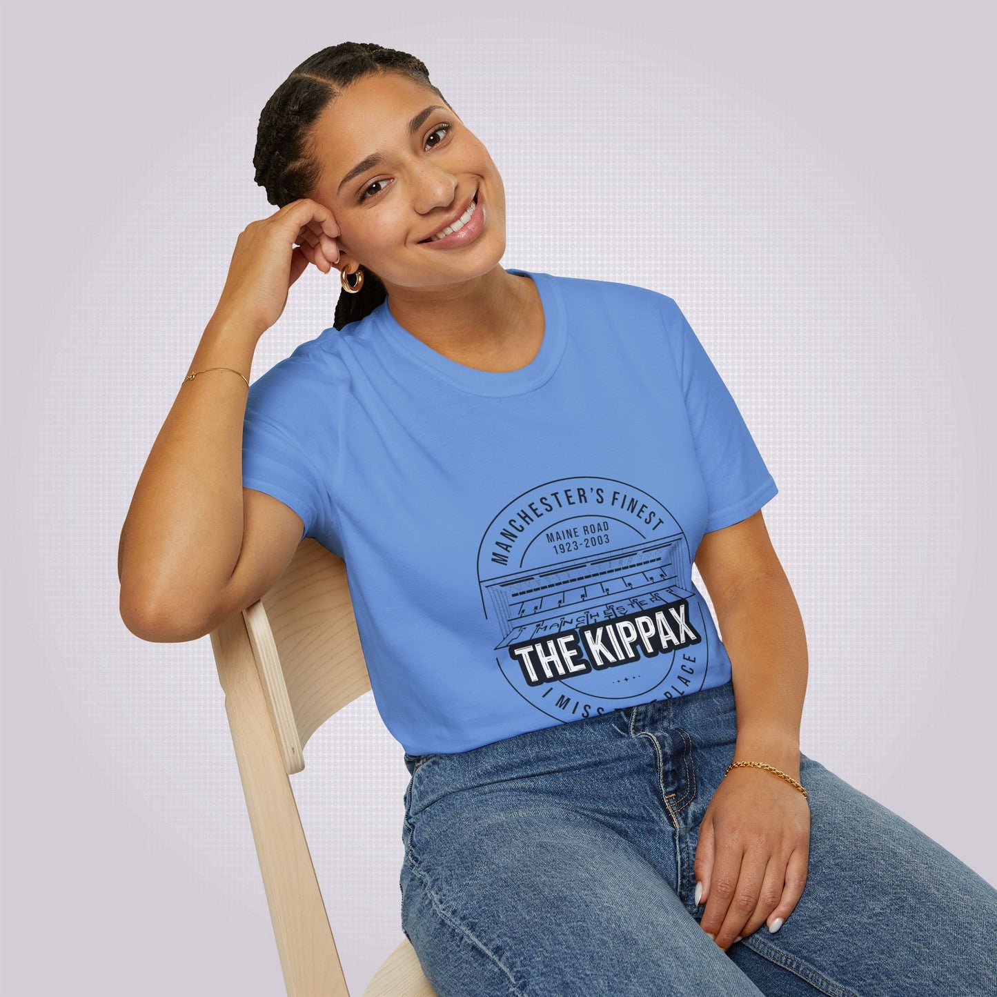 Young mixed race woman sits on a chair leaning against her elbow and smiling at the camera she is wearing the mid blue t shirt with a pair of jeans