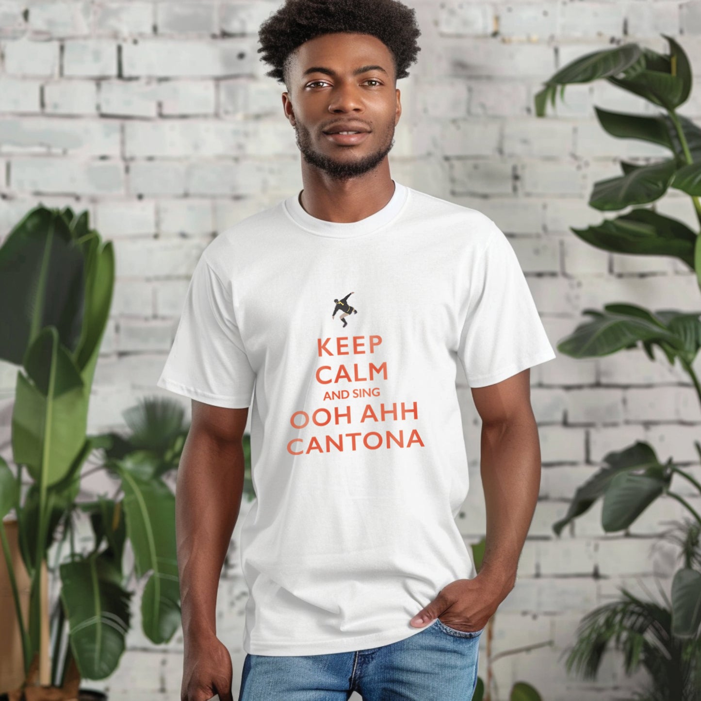 Lifestyle image of a young afro caribbean male in his twenties modelling the white t shirt and jeans he has one hand in his pocket and the other by his side there is a white brick wall and tropical house plants as props blurred out in the background
