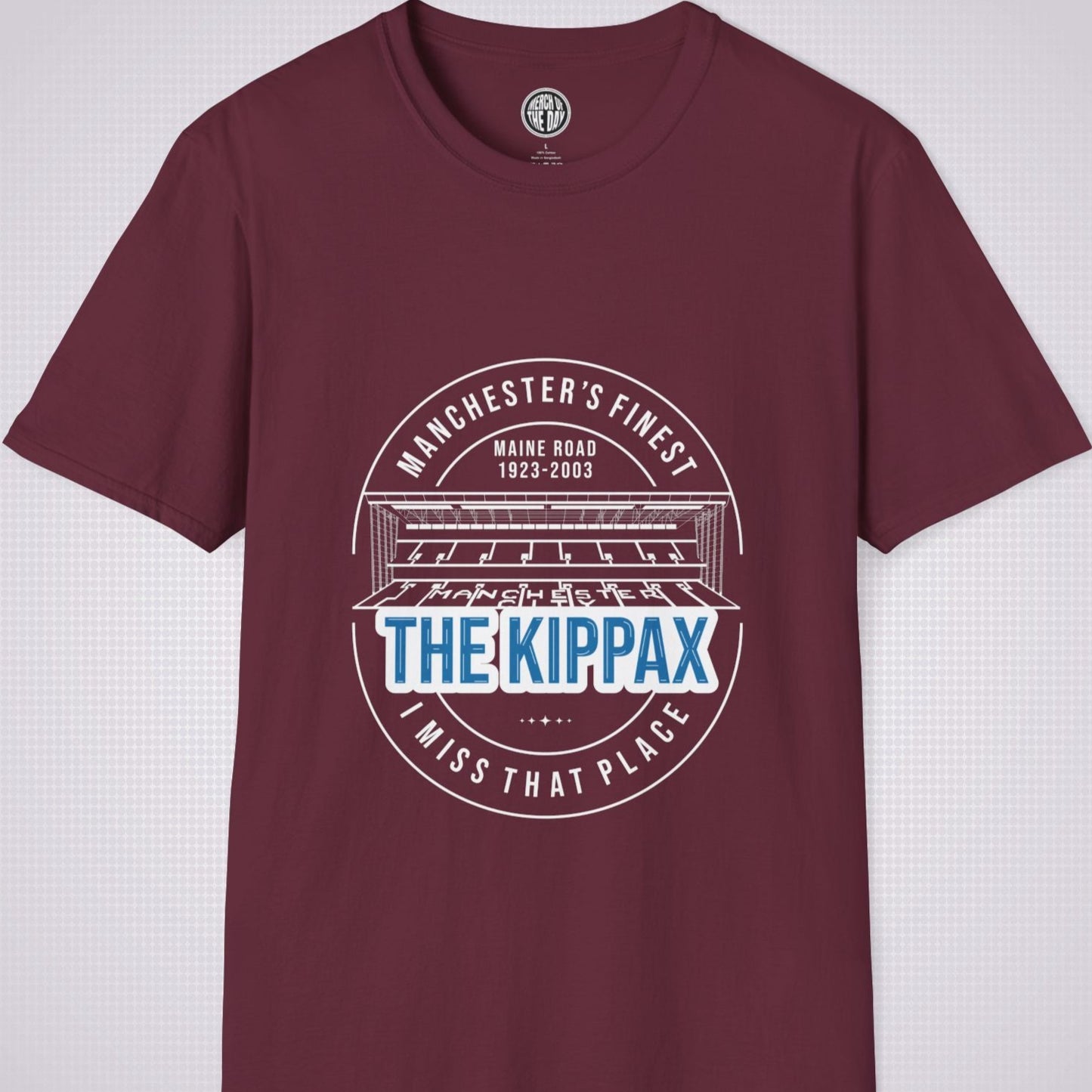 Maroon T Shirt on a light grey dotted background. There is an illustration of the Kippax Stand, above the illustration it reads 'Manchester's Finest Maine Road 1923 to 2003'. Below the illustration it reads 'The Kippax I miss that place'