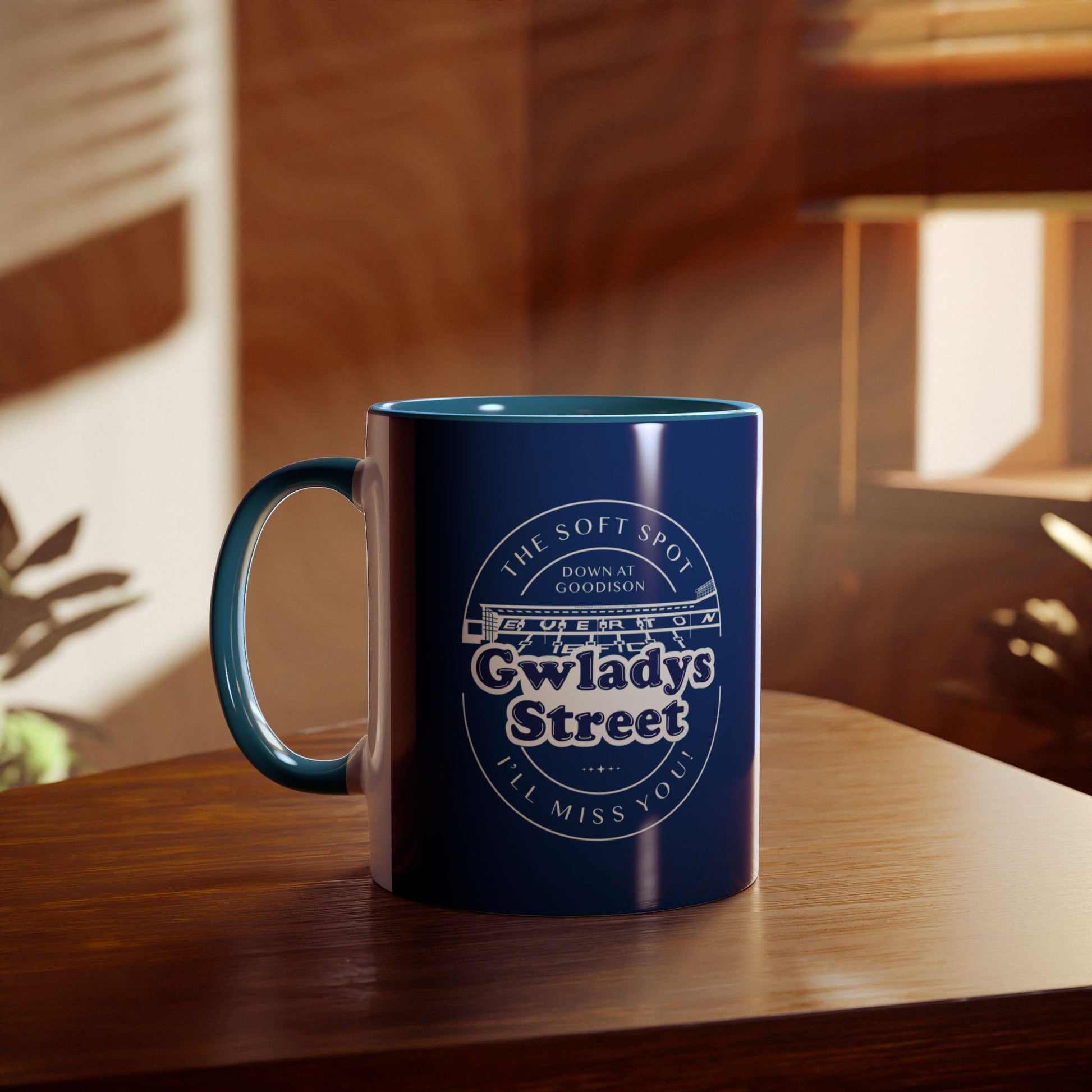 Lifestyle image showing the Navy blue and light blue mug on a wooden table with a blurred living room environment in the background you can see sunlight coming through a window and part of a house plant