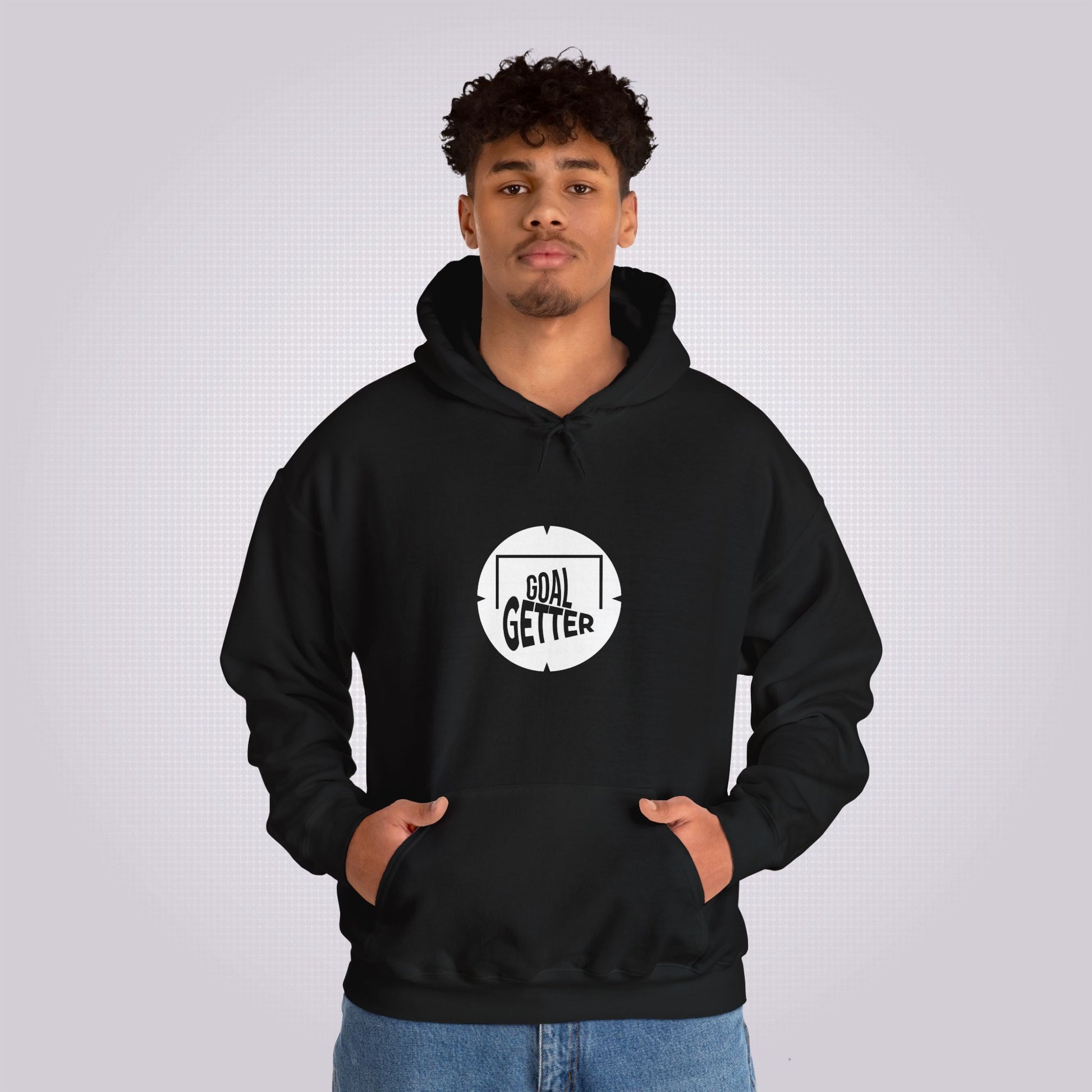 Young mixed race man looks straight at camera as he models the black hoodie and jeans he has his hands in his pockets to demonstrate the pouch design