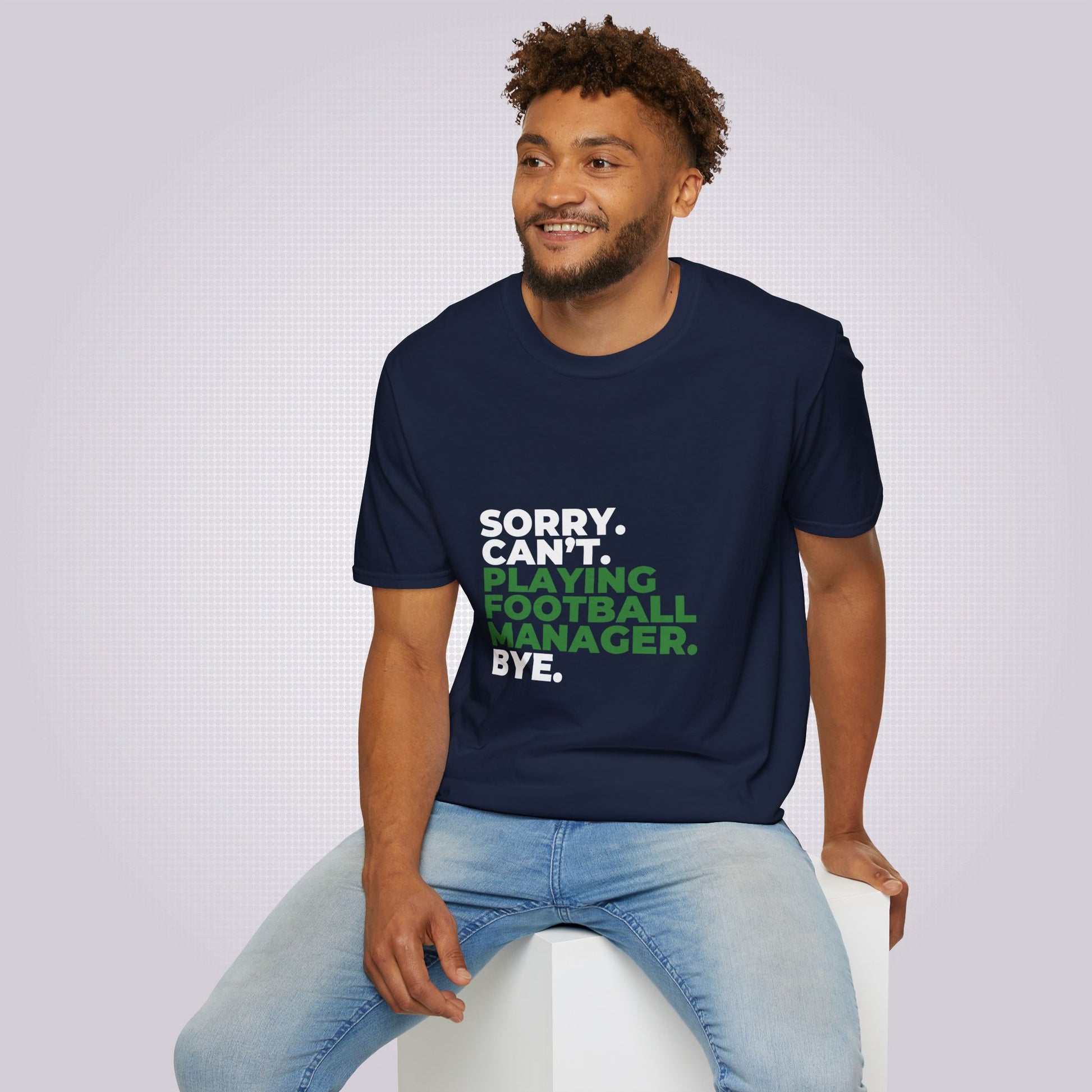 Young mixed race man sits on a white box he is looking off camera and smiling at someone he is wearing the navy t shirt and jeans