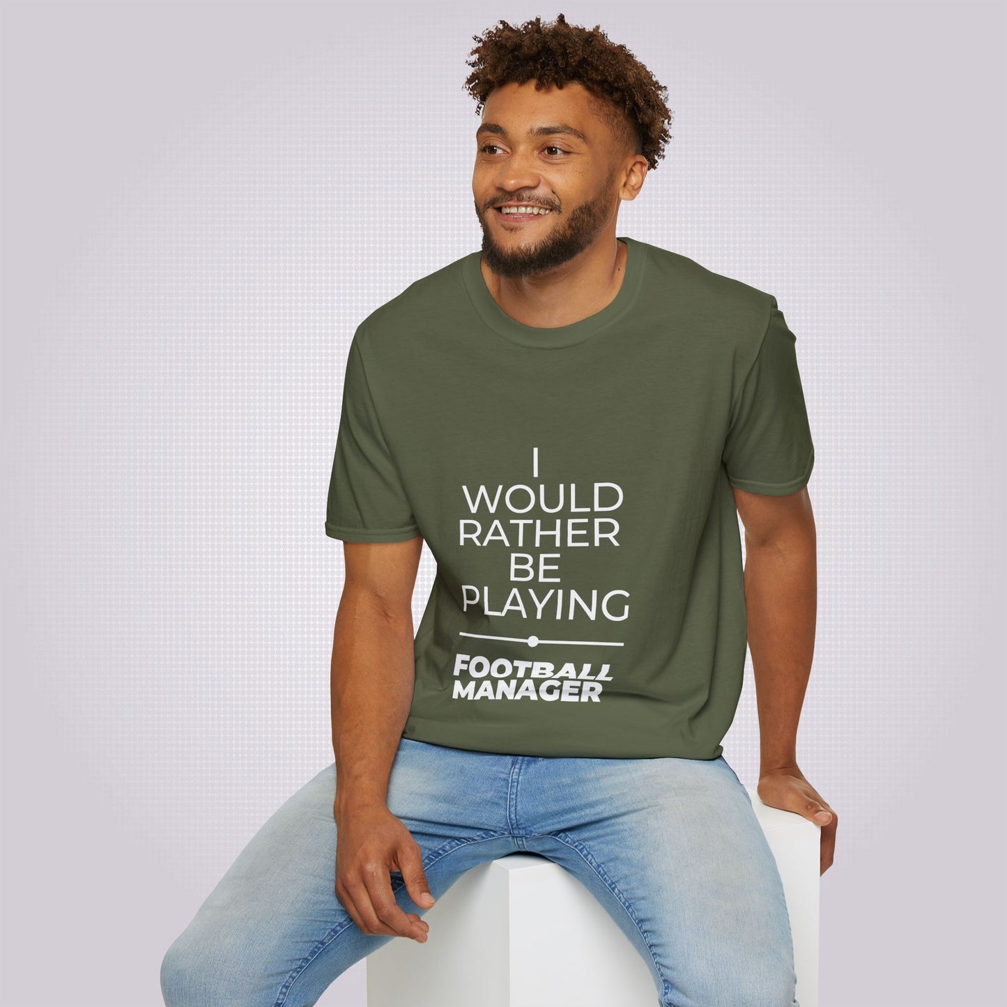 Young mixed race male model sits on a white box smiling away from the camera he is wearing the military green t shirt and jeans