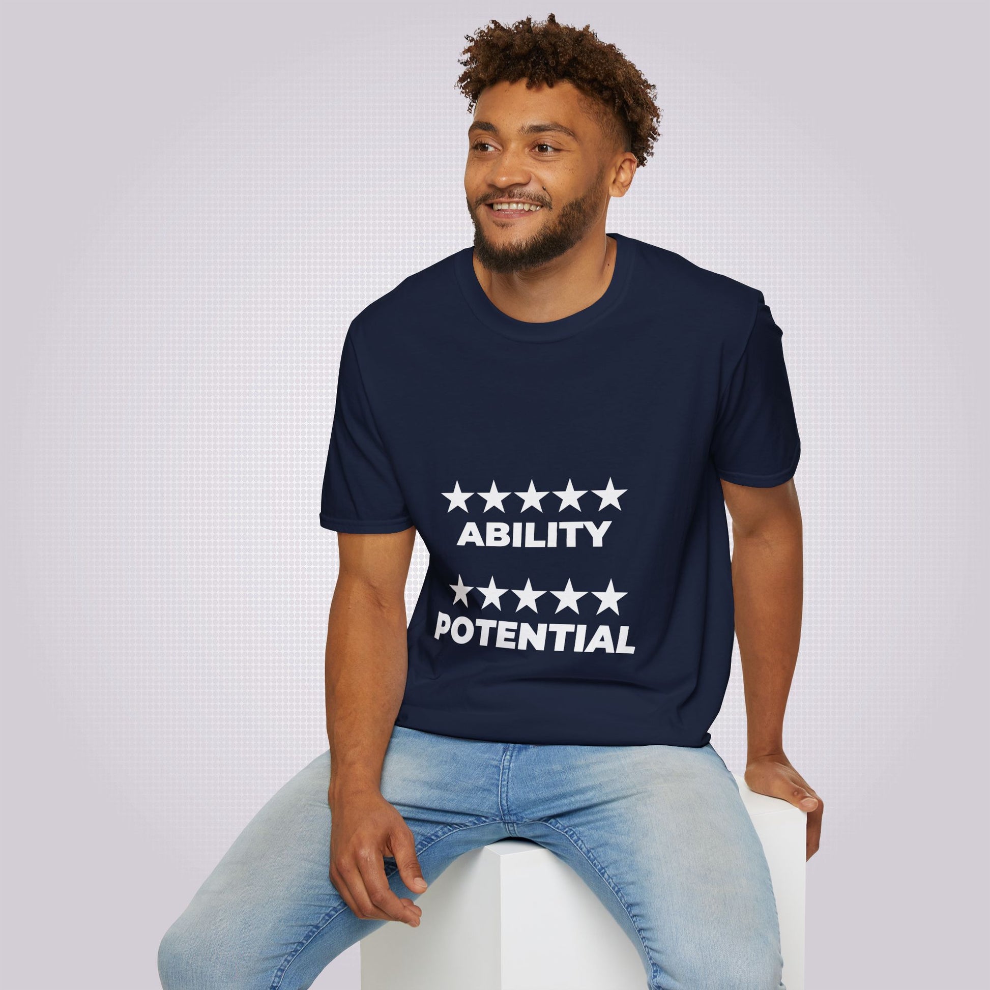 Young mixed race man in his twenties sits on a white box and is wearing the navy t shirt and jeans