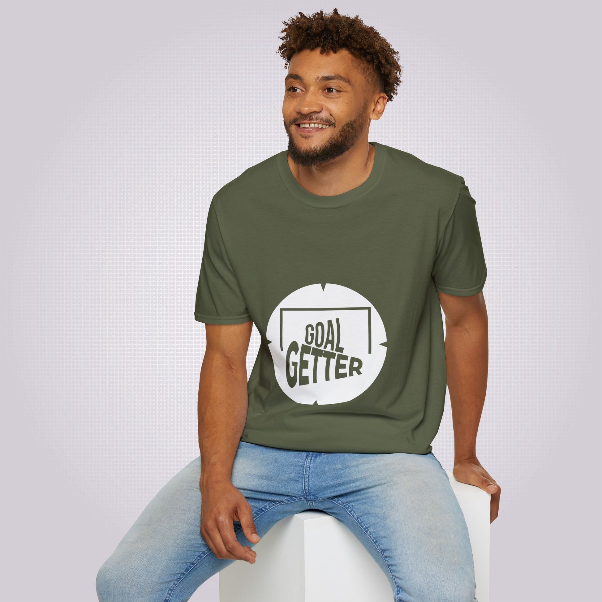 Young mixed race male model sits on a white box while showing off the military green t shirt with a pair of jeans