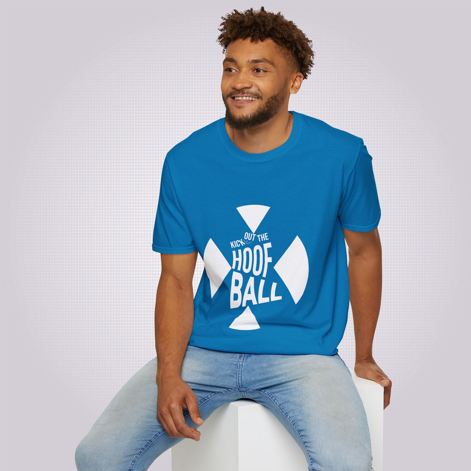 Young mixed race man sits on a white box wearing the Sapphire Blue t shirt with a pair of jeans