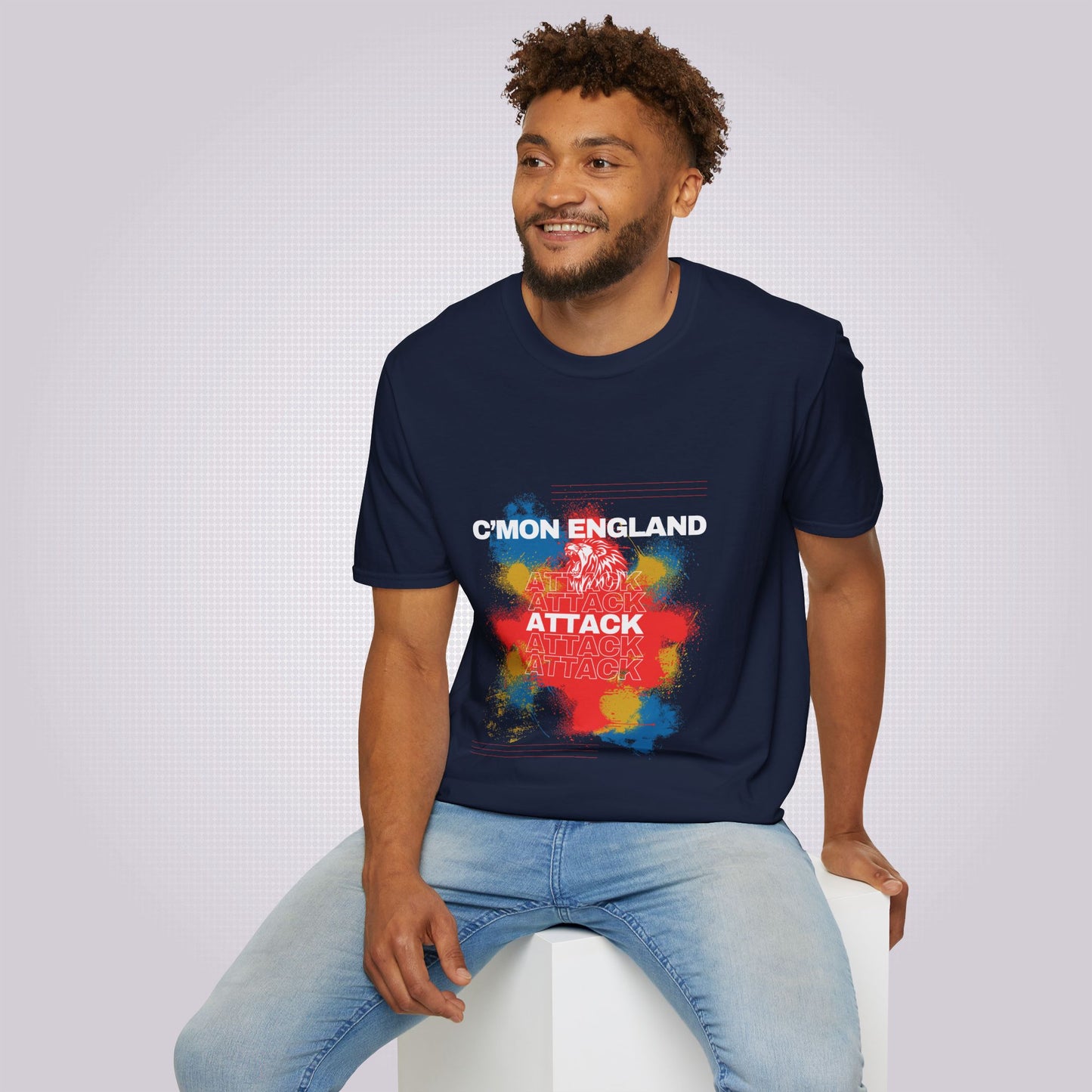 young mixed race man sits on a white box wearing navy t shirt and jeans and he is smiling at someone off camera