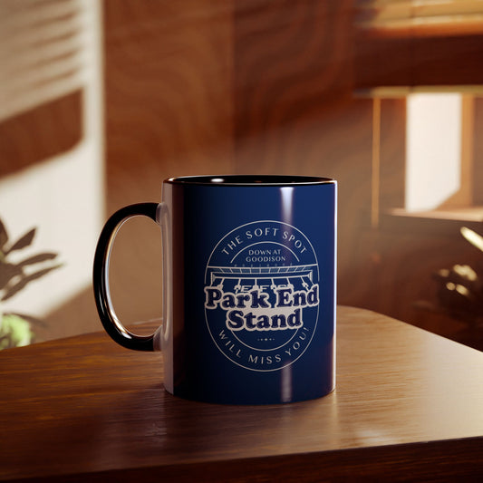 This shows a navy blue mug with a black handle and infill, the handle is on the left hand side. On the front is a graphic showing the Park End stand with the words 'The Soft Spot down at Goodison Park End Stand will miss you'. The mug is placed on a wooden table in what appears to be a study room.