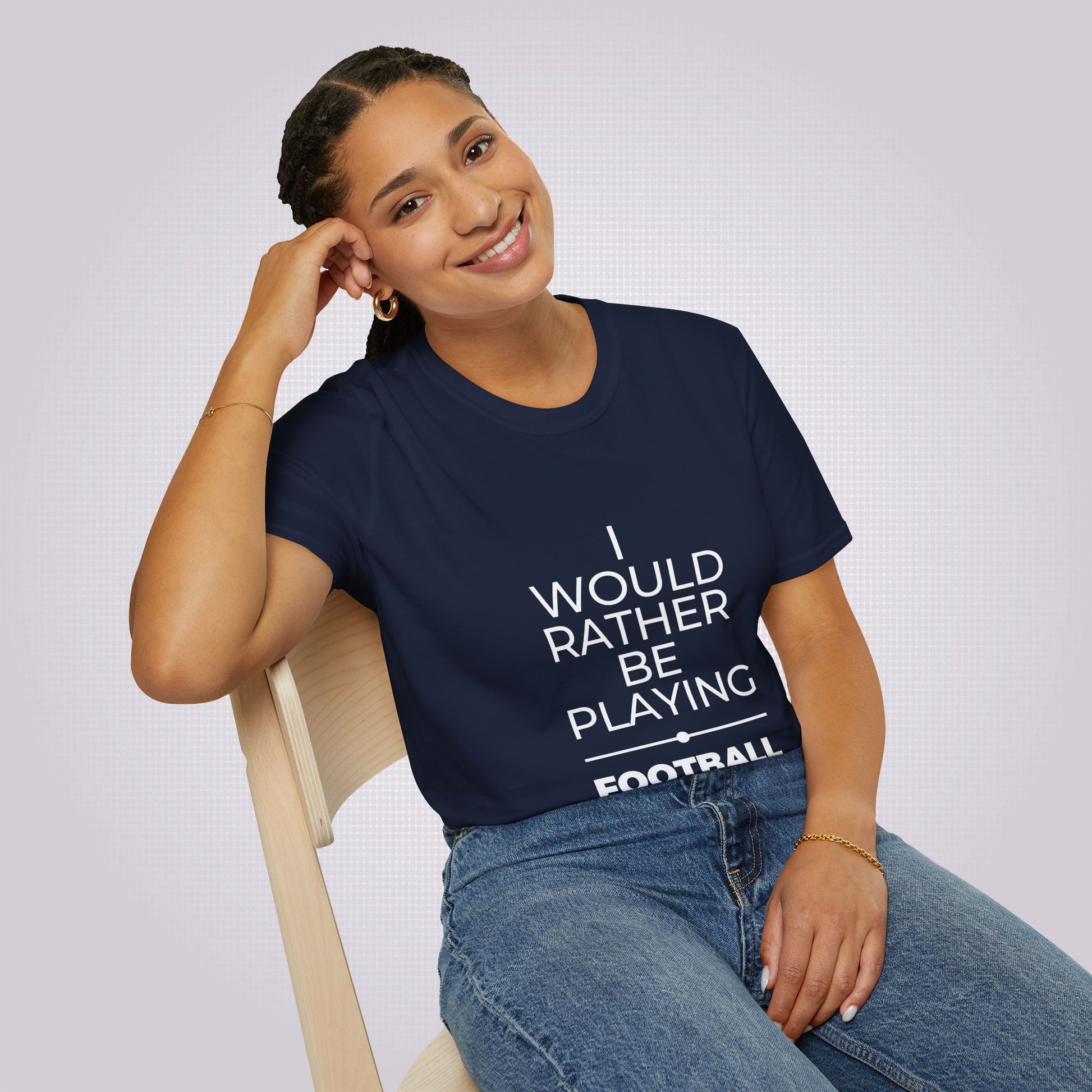 Young attractive mixed race female sits on a chair leaning on her elbow and smiles at the camera wearing the navy t shirt and jeans