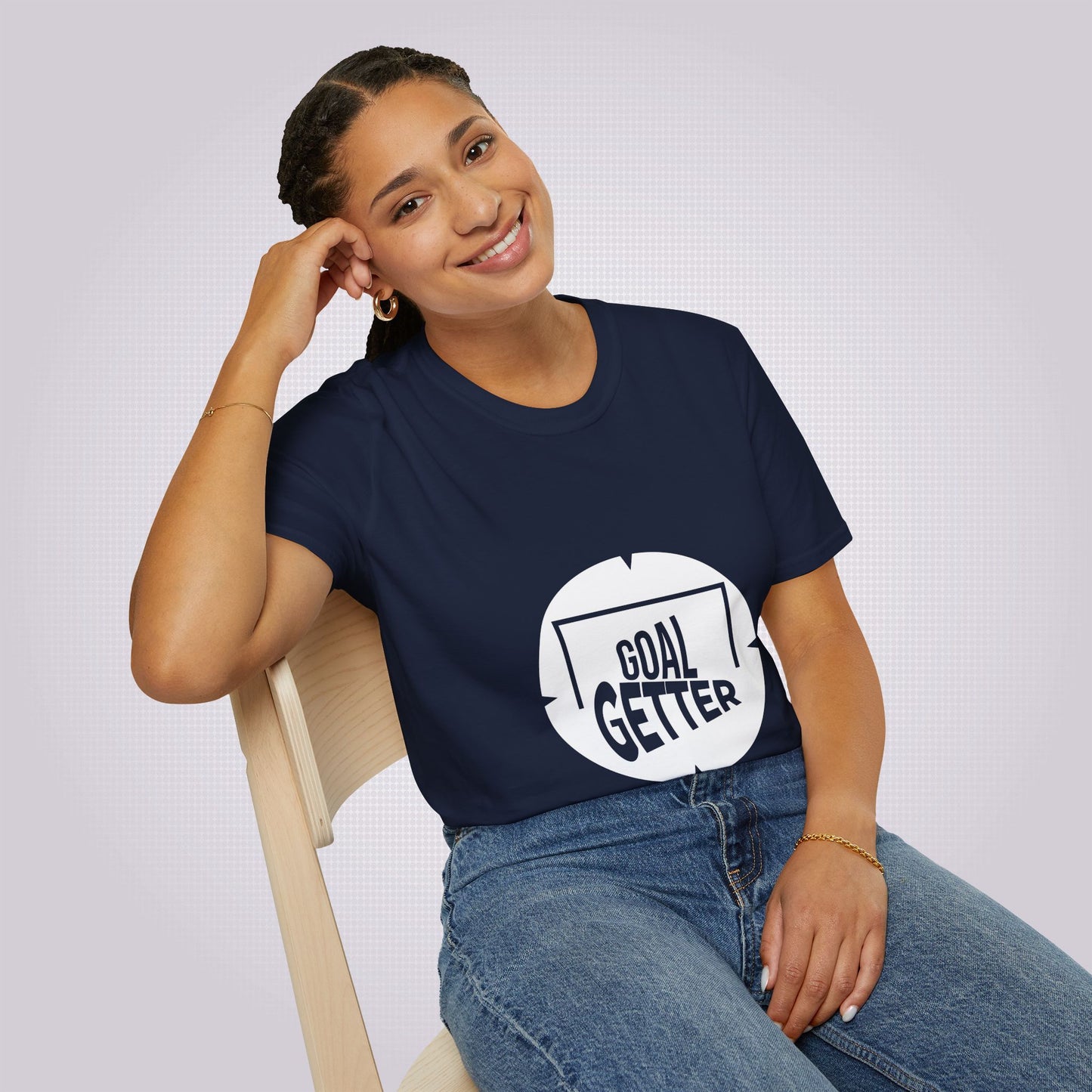 young mixed race lady sits on a chair leaning on her elbow smiling at the camera wearing the navy t shirt and jeans