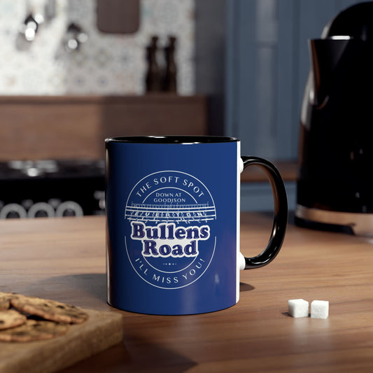 Lifestyle image shows the mug in royal blue with black infill and handle. The mug is on a wooden worktop with two sugar lumps on one side and a wooden board with cookies on to the other side of the mug. Behind the mug is a blurred kettle.