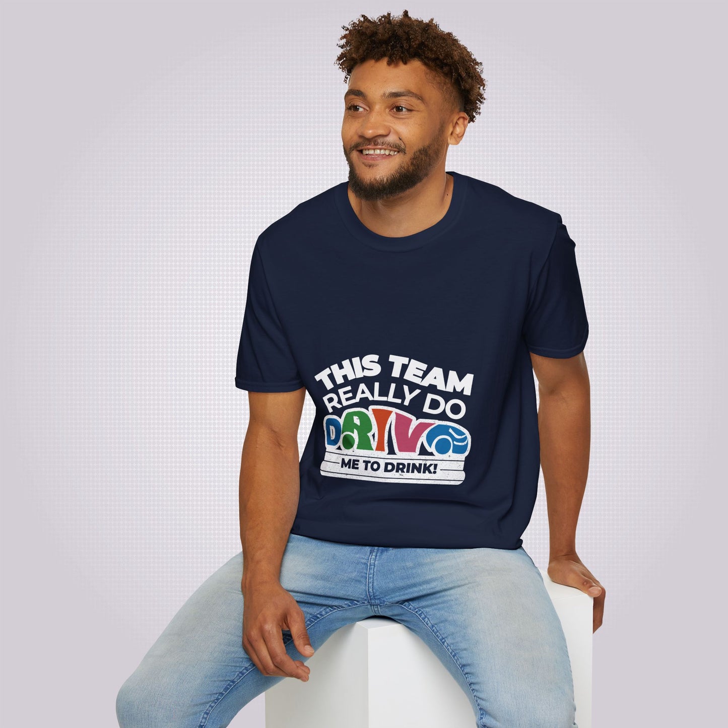 Young male model sits on a white box wearing the navy t shirt and jeans